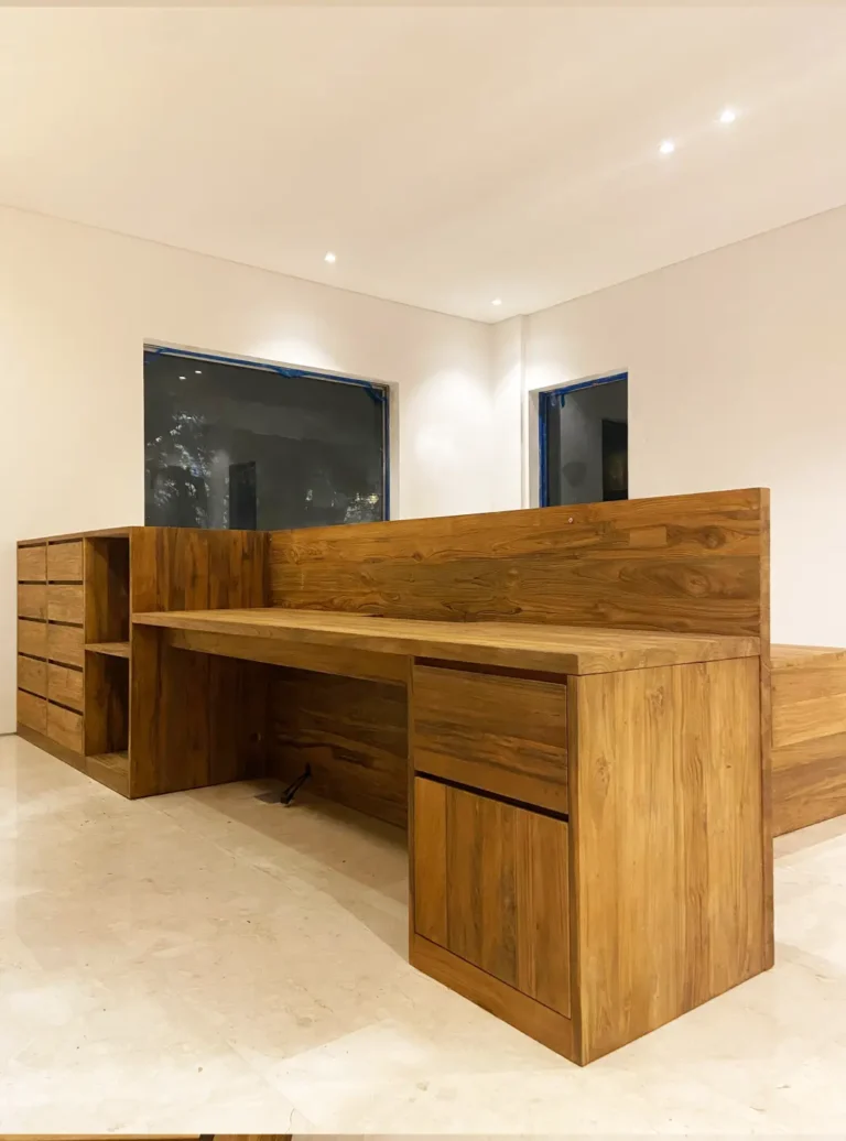 Sebuah meja kerja panjang custom dari kayu jati reclaimed dengan finishing natural, dilengkapi kabinet, banyak laci, dan rak penyimpanan terintegrasi di dalam sebuah ruangan modern minimalis.