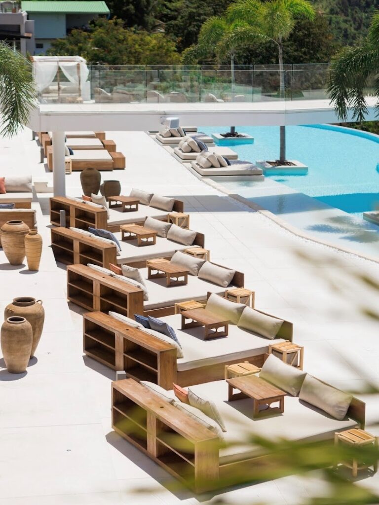 Pemandangan Fira Beach Club di Phuket dengan koleksi furnitur outdoor mewah dari kayu jati daur ulang produksi Permata Furni, menampilkan set sofa dan daybed di tepi kolam renang.