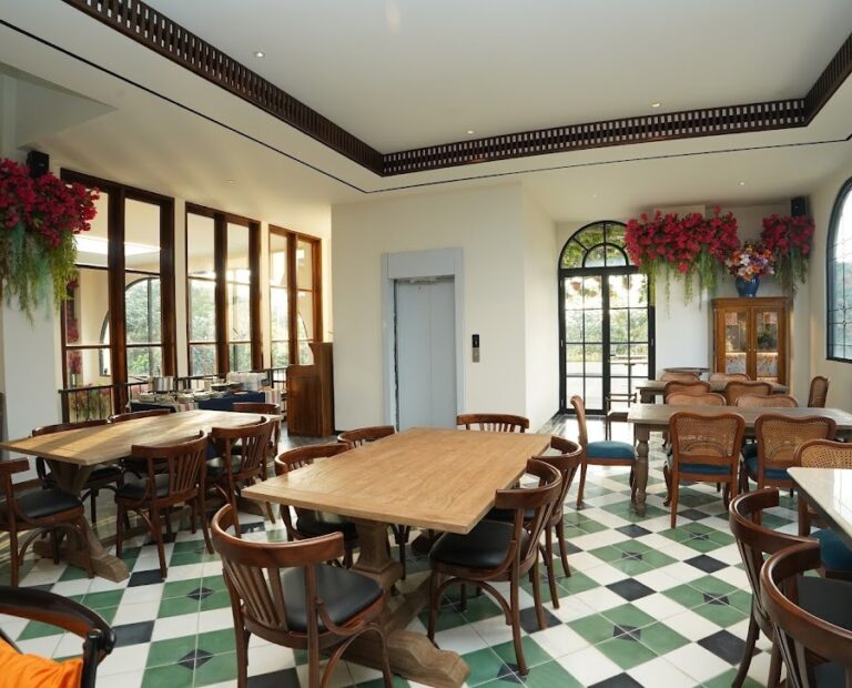 Area makan di Restoran Madame Djeli Bogor dengan pencahayaan alami, menampilkan custom furniture dari Permata Furni berupa meja makan besar dari kayu jati solid model rustic dan kursi makan kayu dengan sandaran melengkung.